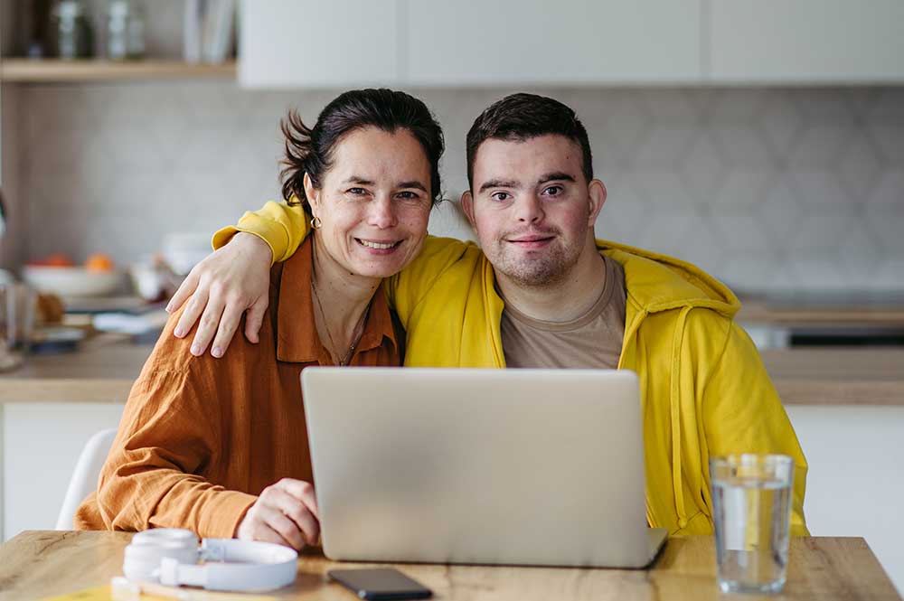 man with down syndrome and mother or caregiver smiling in front of laptop