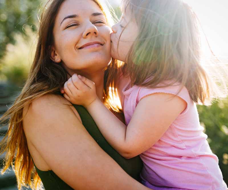 mother smiling, holding her daughter with down syndrome who's kissing her on the cheek